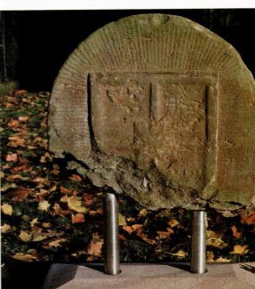 Der restaurierte, bogenförmige Grenzstein von 1772 mit dem verwitterten Wappen der Herrschaft Rheda.