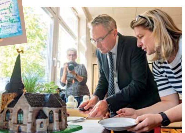 Reinhard Kölsch und Verena Ahnepohl vor einer als Kuchen gestalteten Kirche; Unterschriften am Eingang mit der